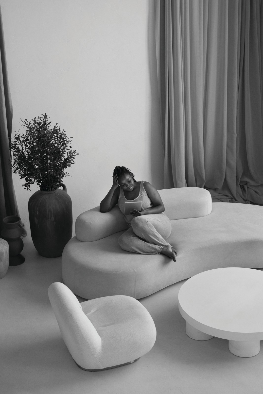 Soft Sculptures – The Art of Curves A woman reclines on a curved white sofa beside rounded sculptural chairs and a low organic coffee table